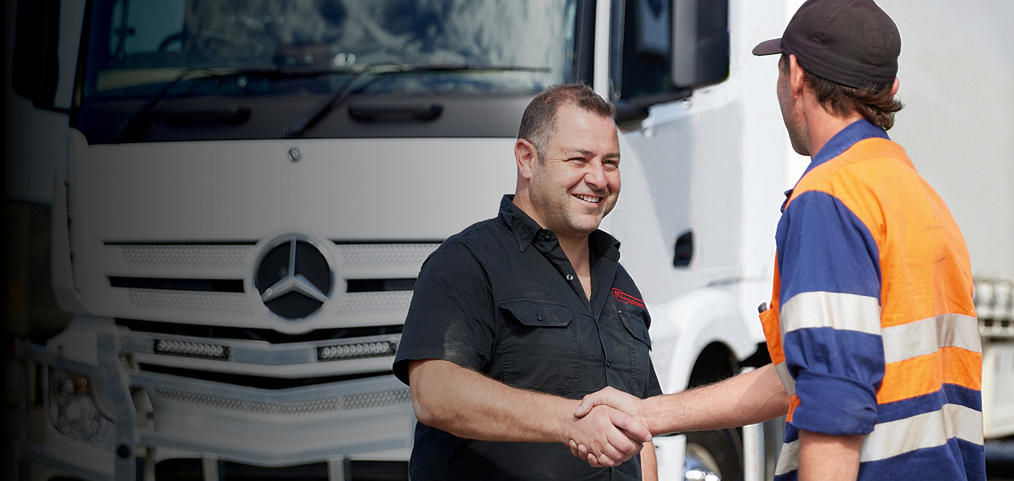 Two people shaking hands in front of a white Mercedes-Benz truck