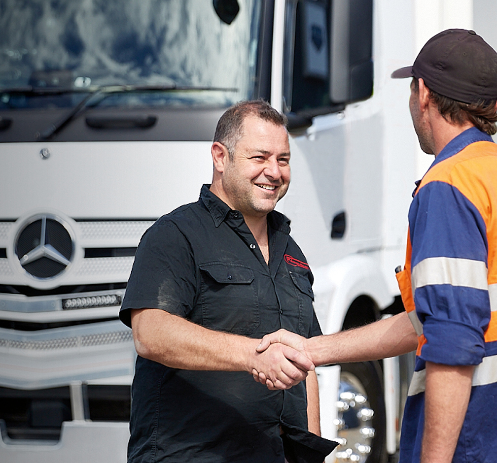 Two people shaking hands in front of a white Mercedes-Benz truck